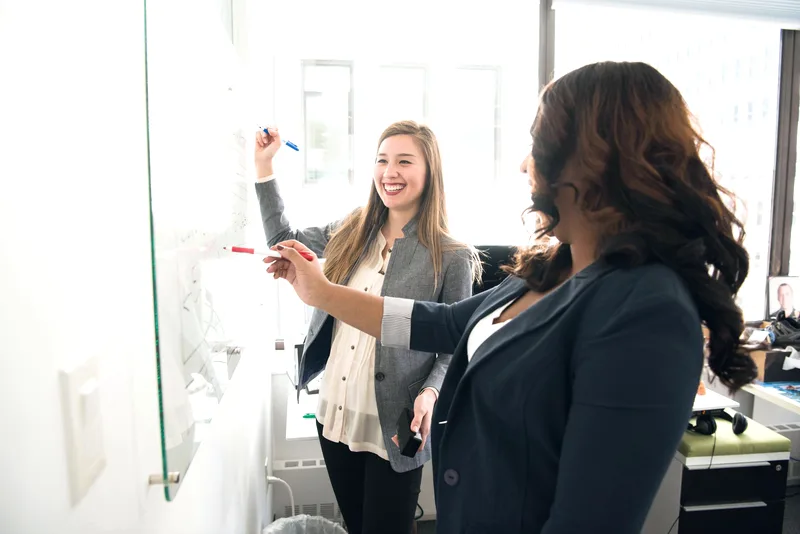 Two colleagues at a sunlit whiteboard — a working session, not a customer portrait
